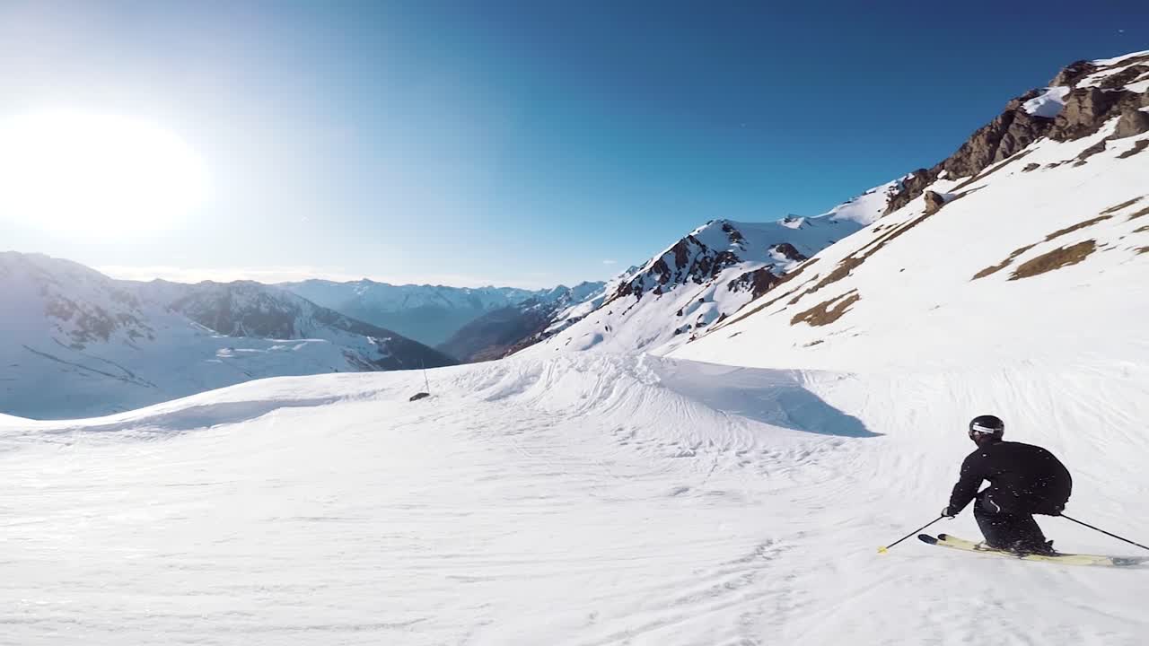 slow motion view of a skier dressed in black gracefully skiing in the mountains with beautiful sunlight rays shining with the beautiful mountain backdrop in the french alps ski resort