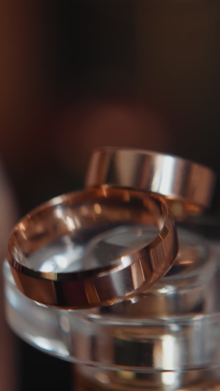 Gleam wedding rings on perfume bottle cap extreme closeup. Gold jewelry accessories and bridal items in room. Matrimonial ceremony preparation