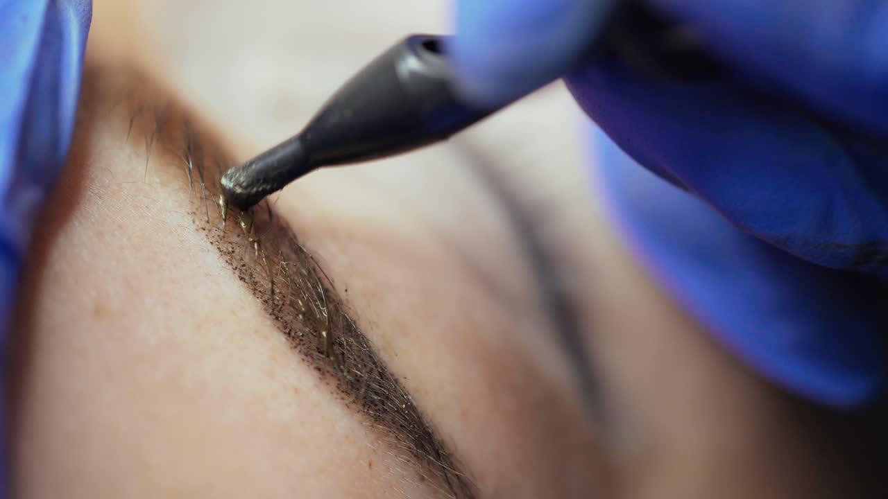 Master's hand is appling tattooing on the eyebrows of a woman with using a professional machine in a beauty salon. Permanent makeup. Close-up