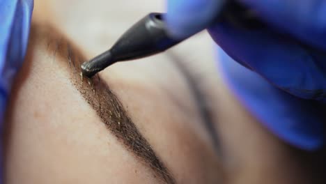 master's hand is appling tattooing on the eyebrows of a woman with using a professional machine in a beauty salon. permanent makeup. close-up