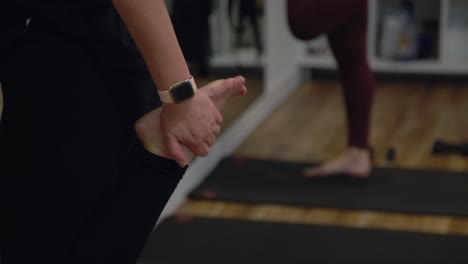 un primer plano de la mano y los pies de una dama haciendo ejercicio en un gimnasio, la dama tiene un reloj inteligente en la mano