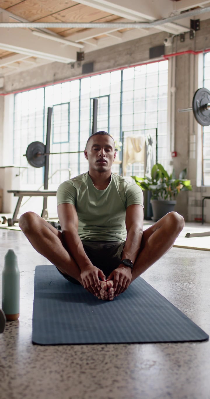 Vertical video: African American man starting butterfly on gym mat adjusting for health bottle left