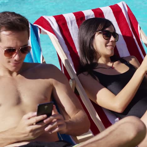 Young-couple-using-phones-at-the-swimming-pool