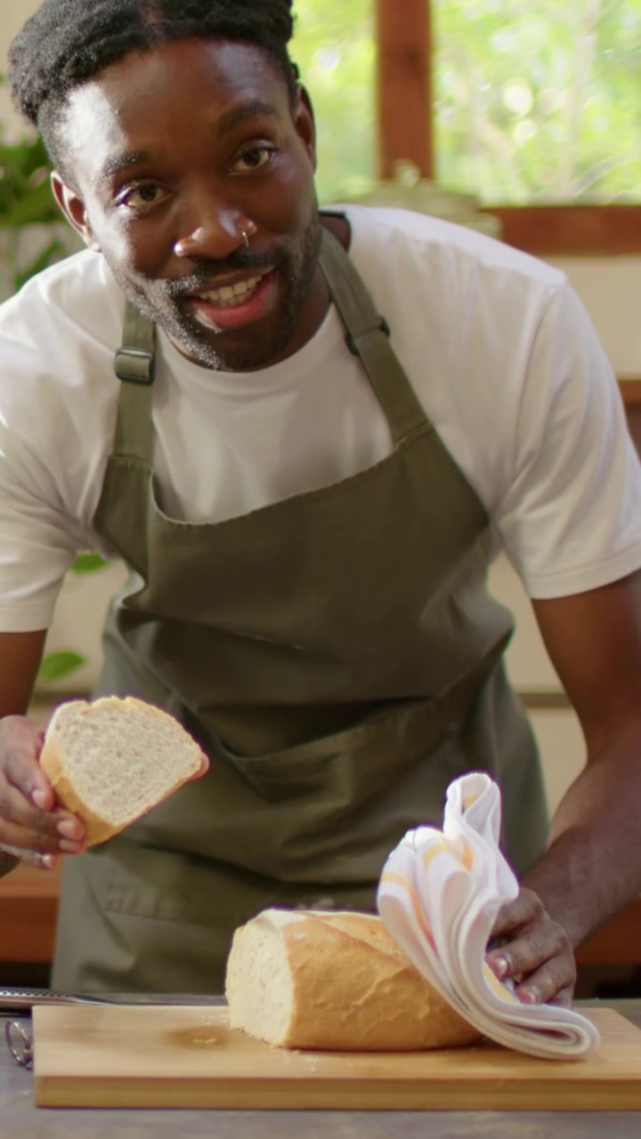 Vertical video: After slicing loaf, man in apron holding slice and showing crumb at home counter
