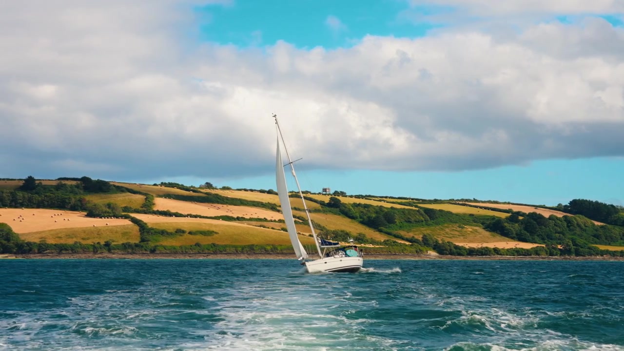 Bootsfahrt zur Entdeckung der kornischen Landschaft im Vereinigten Königreich. Blick auf ein Segelboot und die Heufelder in der Ferne