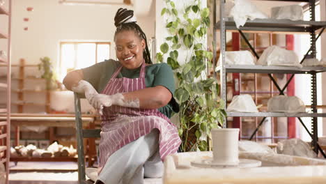 happy african american female potter sitting and smiling in pottery studio, slow motion