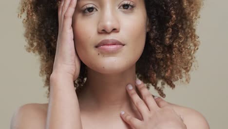 biracial woman with dark hair touching face on beige background, slow motion