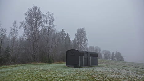 Timelapse-shot-surrounding-a-wooden-cabin-on-a-cloudy-winter-day-with-snow-over-the-field-melting-indicating-arrival-of-spring-in-rural-countryside