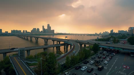 many cars drive bumper to bumper in heavy seoul traffic on gangbyeon expressway and wonhyo bridge over han river during an amazing dramatic sunset in cloudy sky - real time high angle cityscape