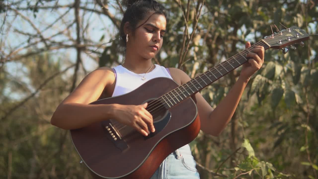 primer plano de una niña india tocando la guitarra durante la puesta de sol con un árbol en el fondo