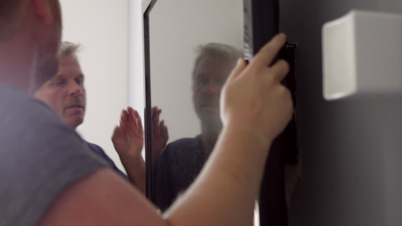 Due uomini che montano un televisore a schermo piatto a parete, ripresi con R3D.