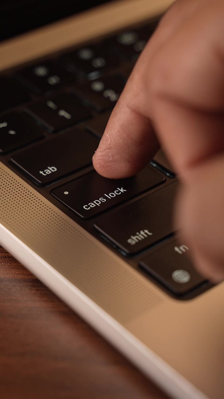Finger trykker på Caps Lock-knappen på bærbar computers tastatur i et varmt oplyst rum