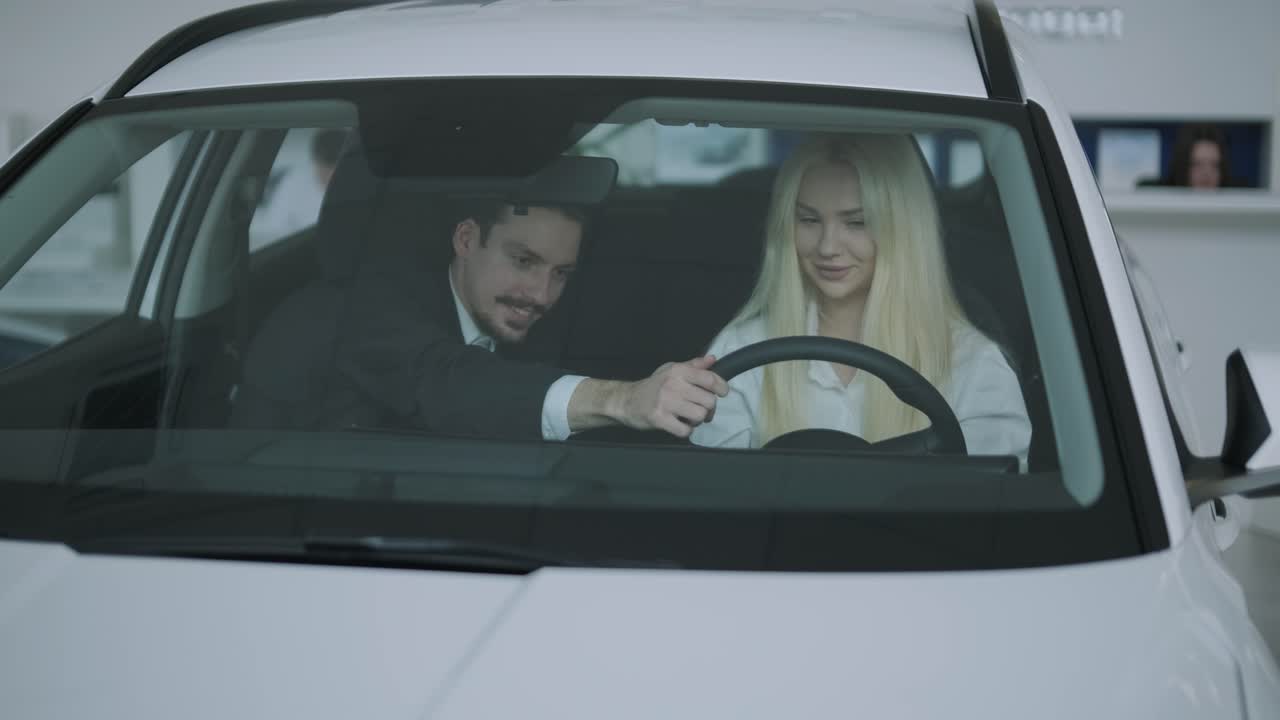 A man and woman in a car at a car dealership