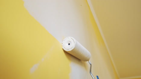 unrecognizable worker painting wall. paint roller with light color in man's hand moving up and down on the wall indoors. room renovation. close-up.