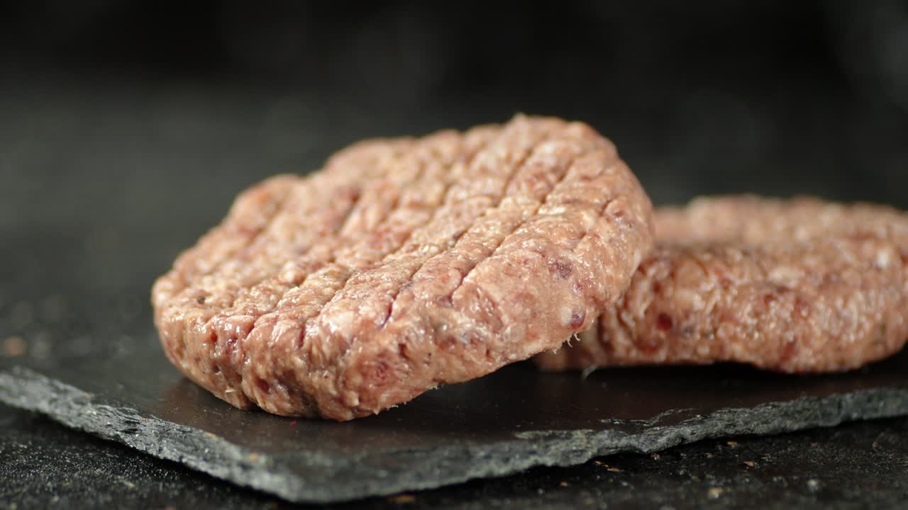 una hamburguesa cruda de carne fresca gira sobre una tabla de piedra.