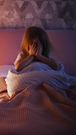 scared little daughter covers face with palms crying on bed with pillows and duvet by decorative children teepee in semidark bedroom at home slow motion