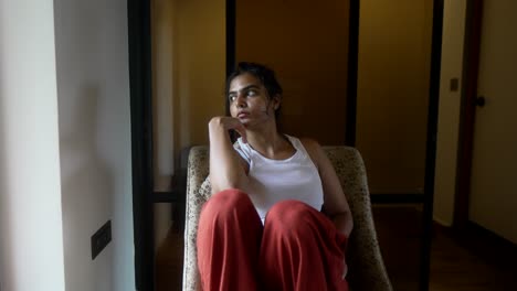 mujer con ropa casual sentada junto a una ventana, mirando pensativamente