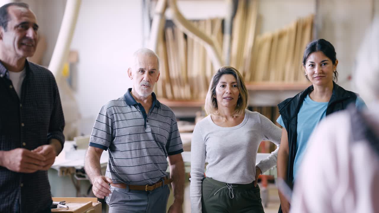 En mångfaldig grupp snickare lyssnar uppmärksamt i en snickeriverkstad.