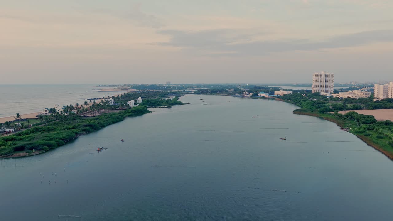 Drone shot of a calm river with lush gvreen vegetation and buildings at bank of either side.