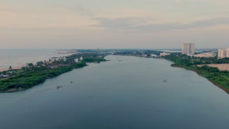 drone shot of a calm river with lush gvreen vegetation and buildings at bank of either side.