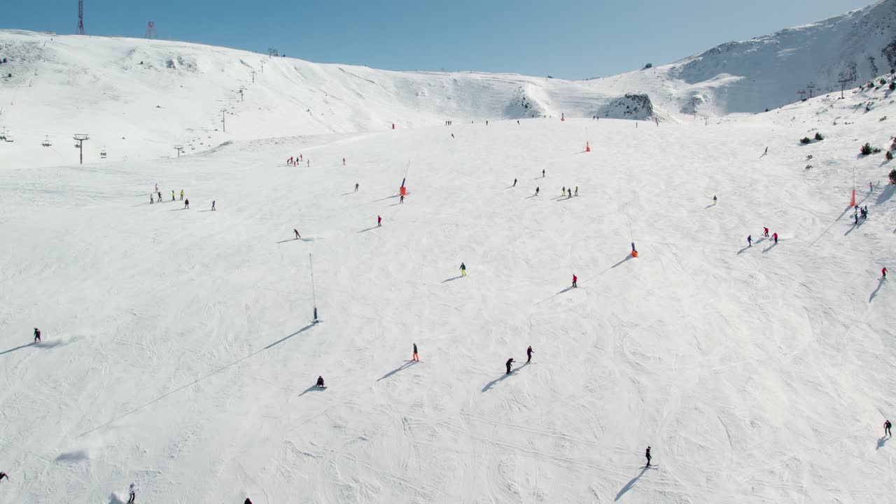 Aerial drone shot flying toward a ski slope with numerous skiers descending in Andorra.
