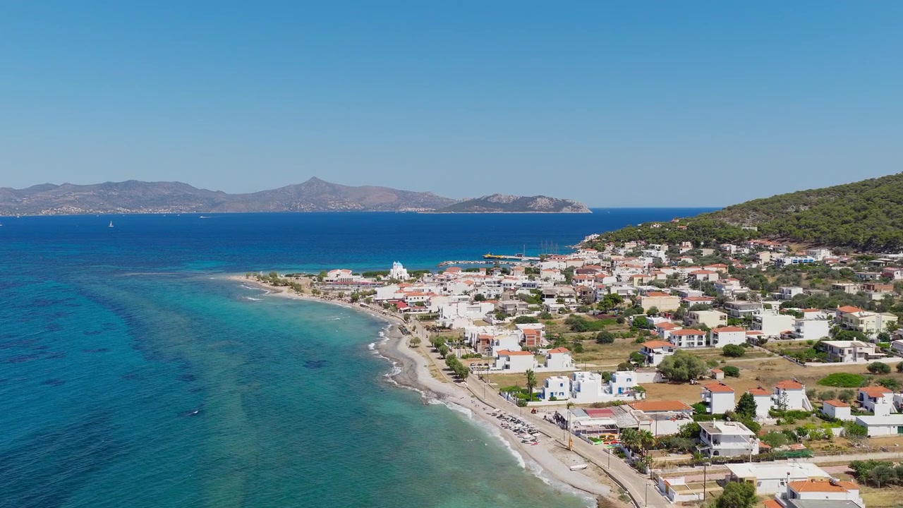 Video drone cattura la vivace costa turchese dell'isola di Agistri e del villaggio di Skala in Grecia, rivelando case imbiancate a calce, mare blu limpido, cieli soleggiati e un paesaggio mediterraneo scenografico