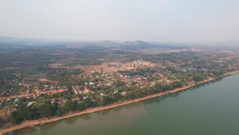 stunning aerial panorama of chiang khan district alongside mekong river on misty morning, drone flying forwards in thailand