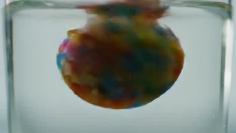 an expansive display of colorful particles swirling in liquid: a mesmerizing journey from a vibrant sphere to an erupting cascade of colorful splinters