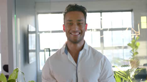retrato de un feliz hombre de negocios biracial inteligente y casual sonriendo en la oficina, en cámara lenta