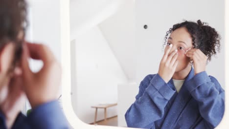 focused biracial woman applying under eye masks looking in mirror in sunny bathroom, slow motion