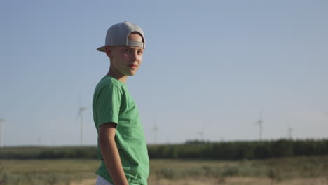 boy in green shirt in field with wind turbines