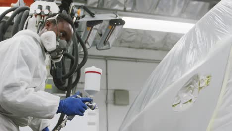 African-American-female-car-mechanic-wearing-protective-clothes-using-a-spraying-gun-to-paint-a-car-