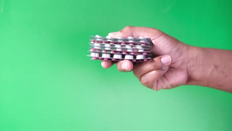 close up of hand holding blister packs against green background