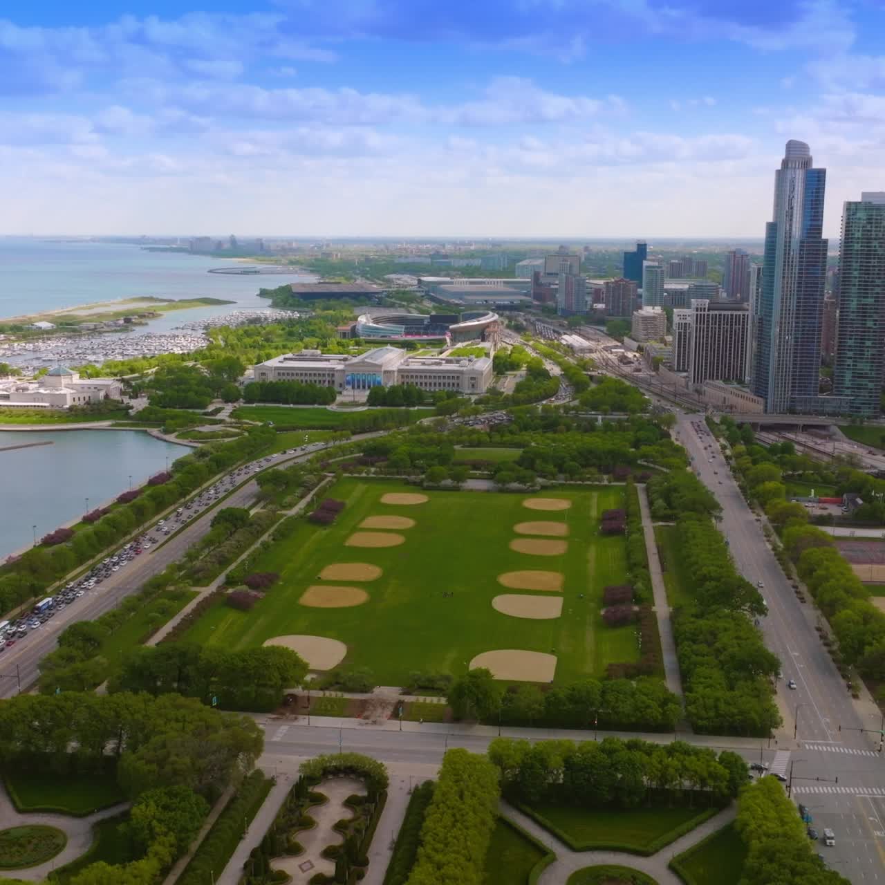 Flying over the wonderful modern park at the lake waterfront. Chicago scenery with skyscrapers at the backdrop of blue cloudy sky