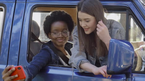 two beautiful girls take a selfie leaning out of the window of a caravan during a roadtrip