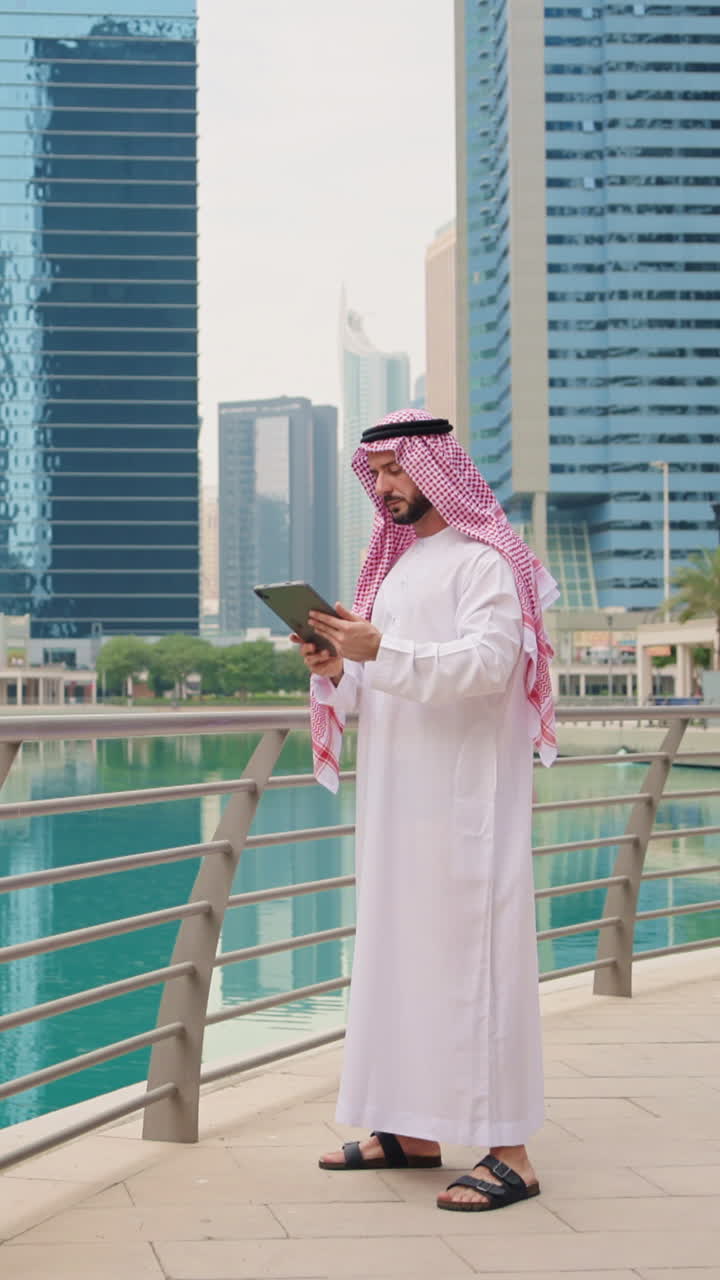 Vertikales Video eines arabischen Professionals in traditioneller Kleidung, der ein digitales Tablet im Geschäftsumfeld verwendet
