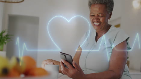 animation of heart shape cardiograph over senior biracial woman using smartphone