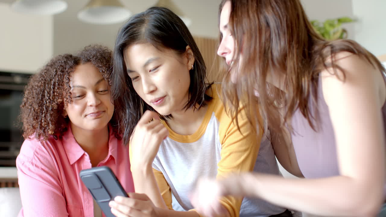 Three women friends looking at smartphone, laughing and enjoying time together at home