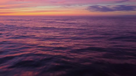 sea waves and ripples with orange sunset sky above, aerial fly forward