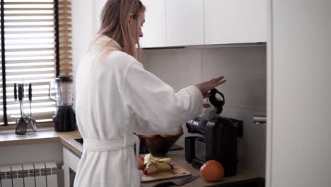 woman in white robe making apple juice in the morning using juicer