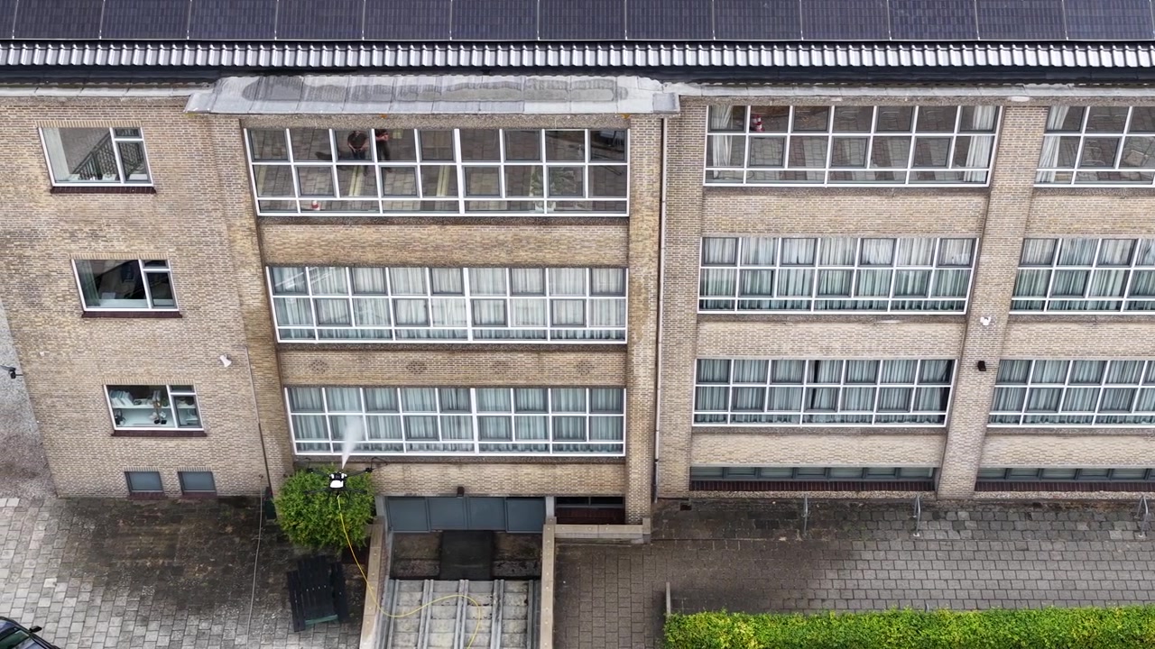 Vista aérea de um UAV lavando janelas em um edifício moderno, exibindo automação, robótica e tecnologia inovadora de limpeza exterior para manutenção de arranha-céus.