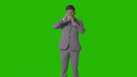 studio shot of businessman in suit holding and drinking cup of hot drink against green screen 1