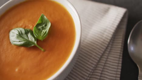 Video-of-cream-tomato-soup-in-bowl-on-wooden-table-with-basil-leaves