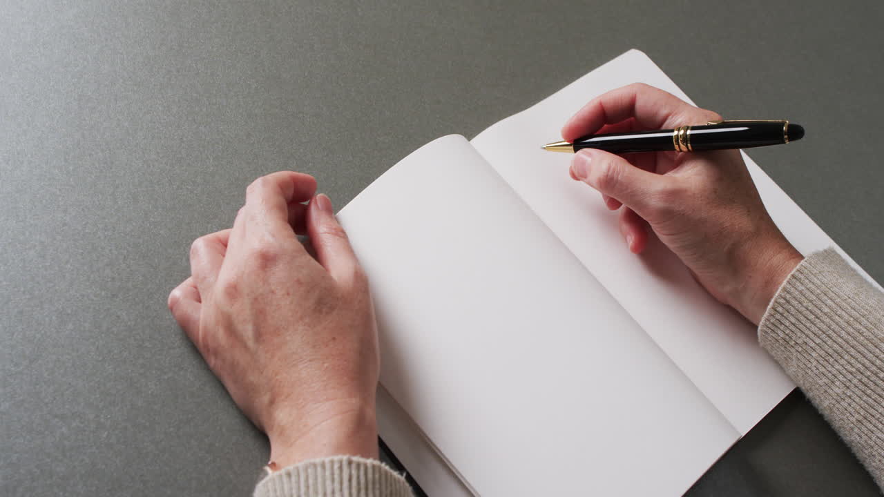 Close up of hands writing with pen on book with copy space on gray background in slow motion