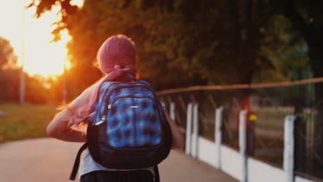 a girl with a schoolbag behind her runs along the alley to the school in the sun back to school