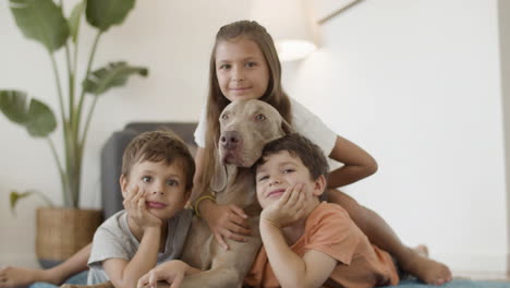 cheerful kids lying with dog on floor and looking at camera