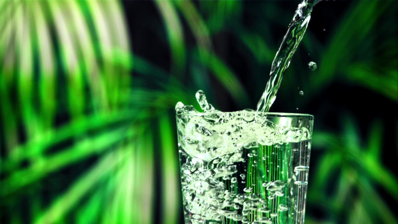 Refreshing Water Poured into a Glass with Green Foliage