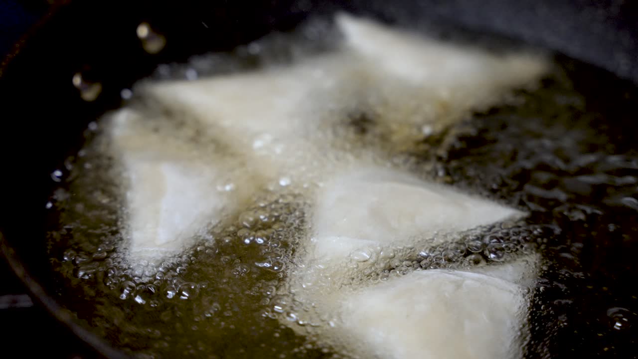 Close up of samosas frying in hot oil, creating bubbles and sizzling sounds, during preparation in a professional kitchen