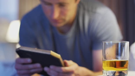 sad man looking at photo sitting on side of bed with glass of whisky on bedside cabinet