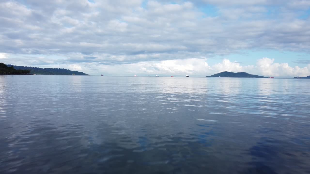 말레이시아 코타키나발루에서 어부 보트를 지나가는 드론이 해수면 근처를 날아다니며 지평선 너머의 큰 선박과 작은 섬을 바라보고 있습니다.